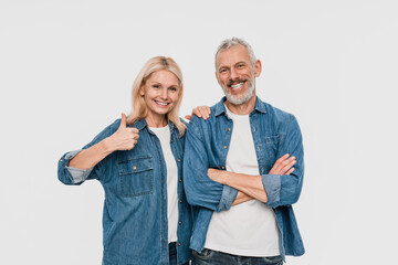 Fototapeta premium Excited cheerful funny couple two friends elderly gray-haired man blonde woman wearing denim casual clothes standing showing thumbs up isolated on white light color background studio portrait