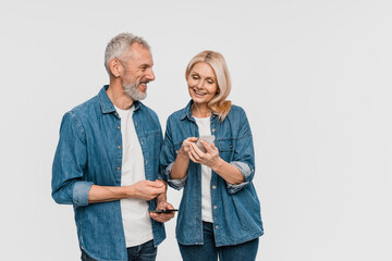 Happy senior couple looking at smartphone screen, elderly man and woman embracing and using using mobile app on cell phone, shopping or banking online, white background copy empty space