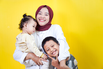 A joyful asian mother holds her two happy children against a bright yellow background. mothers day concept