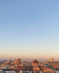 Fototapeta premium Panoramic view of Barcelona at sunset. The warm-colored skyline is dominated by a mixture of historic and modern architecture, including church spires and skyscrapers, and contrasts with the blue sky
