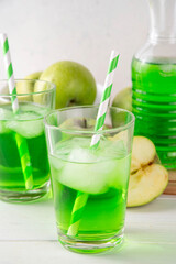 Homemade green apple lemonade cocktail, refreshing summer emerald color drink with fresh green apple juice, a lot of ice and sweet syrup, on white wooden table copy space
