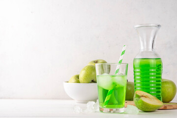 Homemade green apple lemonade cocktail, refreshing summer emerald color drink with fresh green apple juice, a lot of ice and sweet syrup, on white wooden table copy space