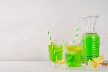 Tarragon summer cold lemonade, green aromatic refreshing cocktail with tarragon syrup or liqueur and lemon, on a white wooden kitchen table