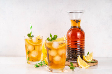 Iced tea cocktail drink, cold summer drink with black tea, lemon, mint and crushed ice, tasty refreshing non-alcohol mocktail on white wooden table background 