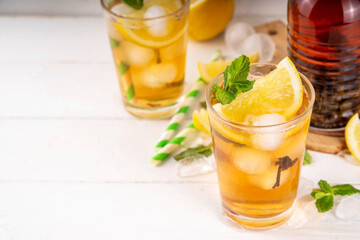 Iced tea cocktail drink, cold summer drink with black tea, lemon, mint and crushed ice, tasty refreshing non-alcohol mocktail on white wooden table background 
