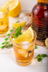 Iced tea cocktail drink, cold summer drink with black tea, lemon, mint and crushed ice, tasty refreshing non-alcohol mocktail on white wooden table background 