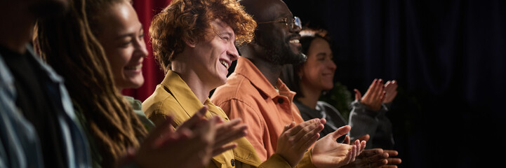 Group of diverse individuals clapping enthusiastically while enjoying event in indoor setting....
