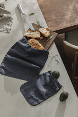 Sliced bread on wooden board, avocado, fresh herbs, linen towel and stainless still kitchen knife. Kitchen aesthetic concept