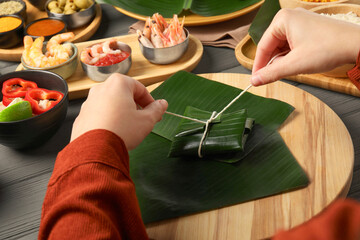 Woman tying banana leaf with food at wooden table with products, closeup. Healthy eco serving