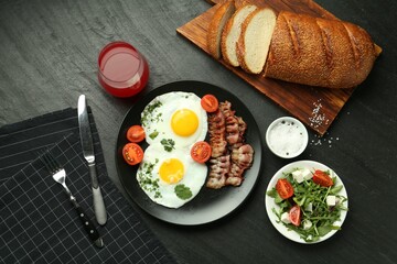 Tasty brunch. Delicious fried eggs, bacon, salad and glass of juice served on black table, flat lay