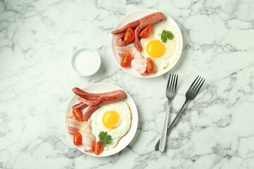 Tasty brunch. Fried eggs, sausage, bacon and tomatoes served on white marble table, flat lay