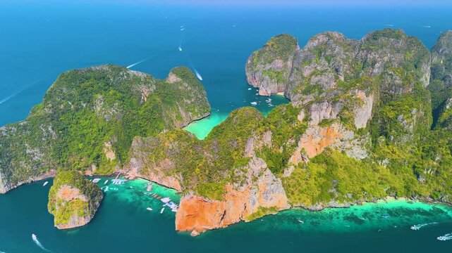 Aerial panoramic beautiful view from afar of Phi phi island ring of steep limestone cliff hills surrounding Maya Bay white beaches and coral reefs around, boats floating nearby