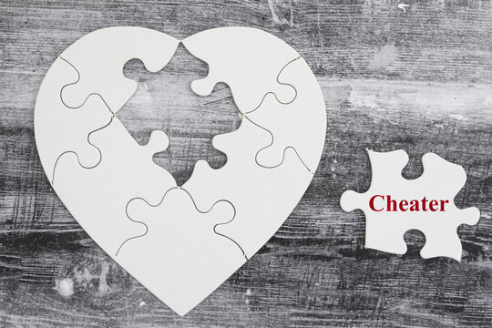 Broken puzzle heart with word cheater on weathered wood