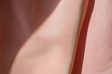 Close-up of peach fuzz-hued suede leather, velvety, smooth surface with subtle shadows.