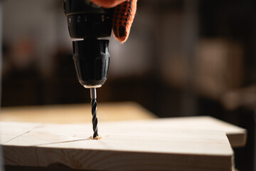 Close-up of carpenter using electric drill. Joiner drilling wood plank on table. Joinery work and...