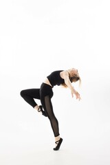 Dancer in black attire performs a graceful pose against a bright background in a studio setting