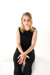 Fototapeta premium Young woman in black attire seated on a white surface, her expression focused and contemplative, minimalistic background enhances her presence