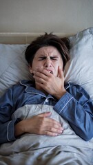 Fototapeta premium Woman in pajamas lying in bed shows signs of exhaustion and discomfort during morning wake up routine
