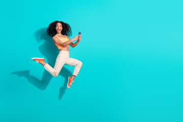 Happy stylish woman jumping with excitement on a turquoise background holding smartphone
