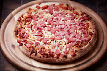 Pizza with ham and mozzarella cheese on wooden background. Soft focus. Close up	