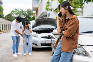 Asian Woman drivers call insurance after a car accident before taking pictures and sending insurance. Car Accident Emergency, while another person tends to a passenger with an injury.
