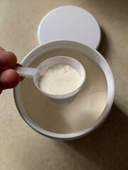 Collagen protein powder in a transparent plastic scoop, held above an open container, showing fine granular texture