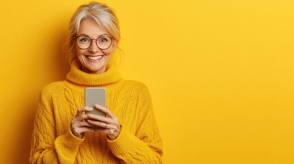 Smiling woman in a yellow sweater holding a smartphone against a bright yellow background during a cheerful moment