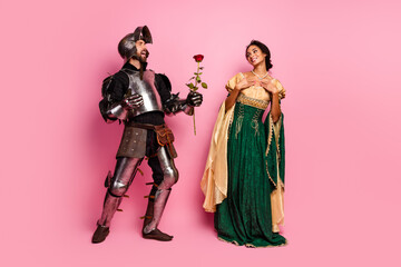 Medieval themed couple with knight's armor and elegant gown on pink background