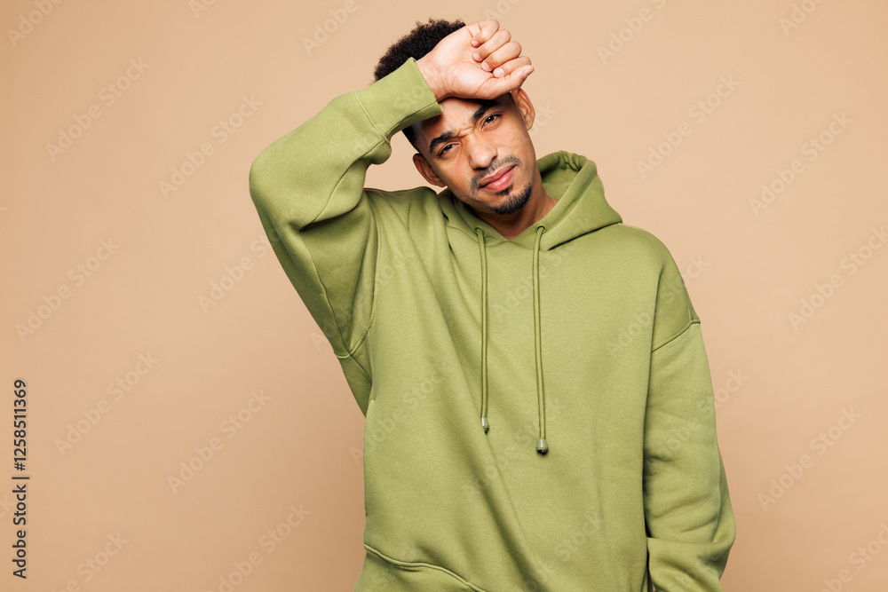 Wall mural Young sad sick man of African American ethnicity wear green hoodie casual clothes put hand on forehead suffer from headache isolated on plain pastel light beige background studio. Lifestyle concept.