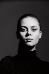 Confident young woman with long hair in a black turtleneck, gazing sincerely at the camera against...