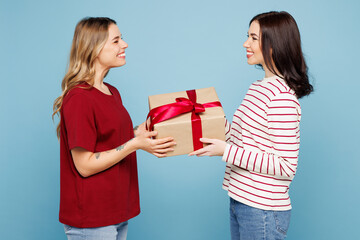 Side view young couple two friends women wearing red casual clothes together holding present box with gift ribbon bow isolated on pastel plain light blue background studio portrait. Lifestyle concept.