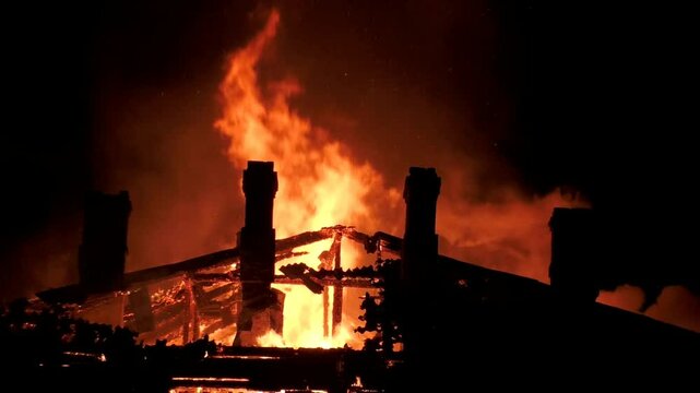 The house is on fire from inside and outside with large flames, flaming doors and windows. The great fiery misfortune of people. Fire rescue at night of the building.