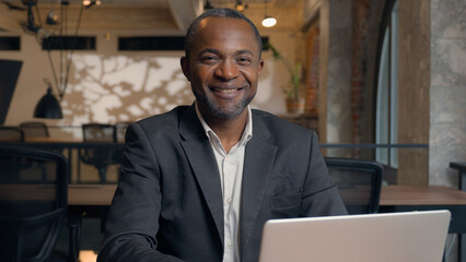 Smiling at camera African American middle-aged entrepreneur typing laptop computer ethnic business...