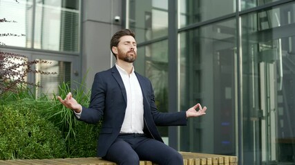 Businessman in formal suit meditating with closed eyes sitting on a bench on the street near an office building. Calm worker practices yoga outside, feels peace of mind. Male relaxes to relieve stress