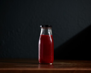 Red Cold-pressed juice bottle on wooden table with dark background