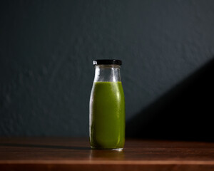 Green Cold-pressed juice bottle on wooden table with dark background