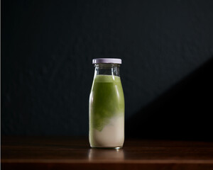 Matcha latte with nut milk bottle on wooden table with dark background