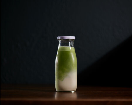 Matcha latte with nut milk bottle on wooden table with dark background