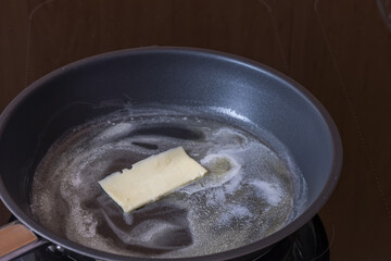 The pan is on the stove and the butter is melting on it.