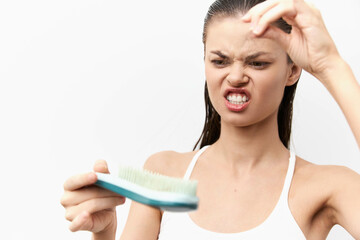 frustrated woman examining hairbrush with hair strands, stressed expression, against plain white...