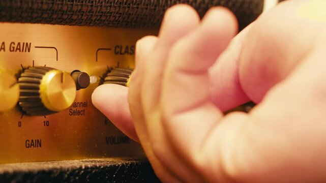 Close-up of plugging a jack into a guitar amplifier and turning up the volume knob, live concert show, playing music on guitar tube amplifier.