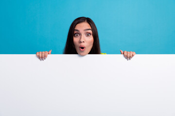 Excited Young Woman Looking Surprised While Holding a White Board Against a Bright Blue Background