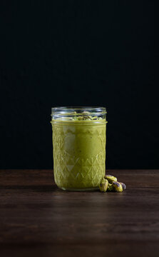 Pistacio Butter in glass jar with nuts on wooden table dark background