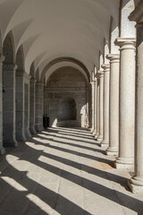 Interior of a gallery with columns and semicircular arches casting their shadows in the monastery of El Escorial. Spain