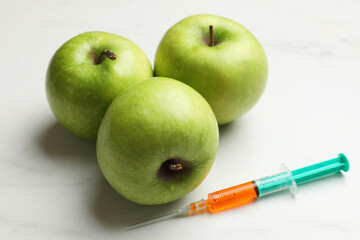 GMO concept. Green apples and syringe on white marble table, closeup