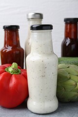 Tasty sauces in glass bottles and fresh products on light grey table, closeup