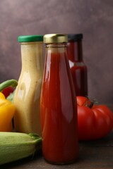 Tasty sauces in glass bottles and fresh products on wooden table, closeup