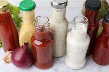 Tasty sauces in glass bottles and fresh products on white marble table, closeup