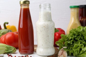 Tasty sauces in glass bottles and fresh products on white wooden table, closeup