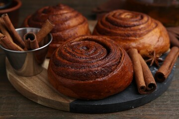 Delicious cinnamon roll buns and spices on wooden table, closeup